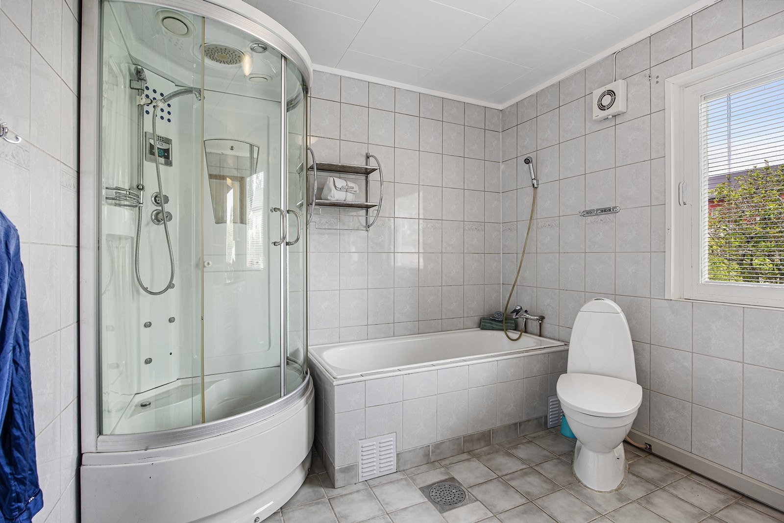 Varme er lagt under gulvet, og badet har toalett, et hvitt servantskap, to matchende veggskap og et speil med belysning over servanten. Galleribilde