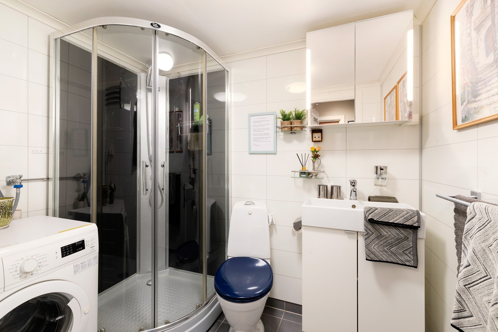 Flislagt bad som inneholder dusjkabinett, servant, wc og opplegg for vaskemaskin Galleribilde