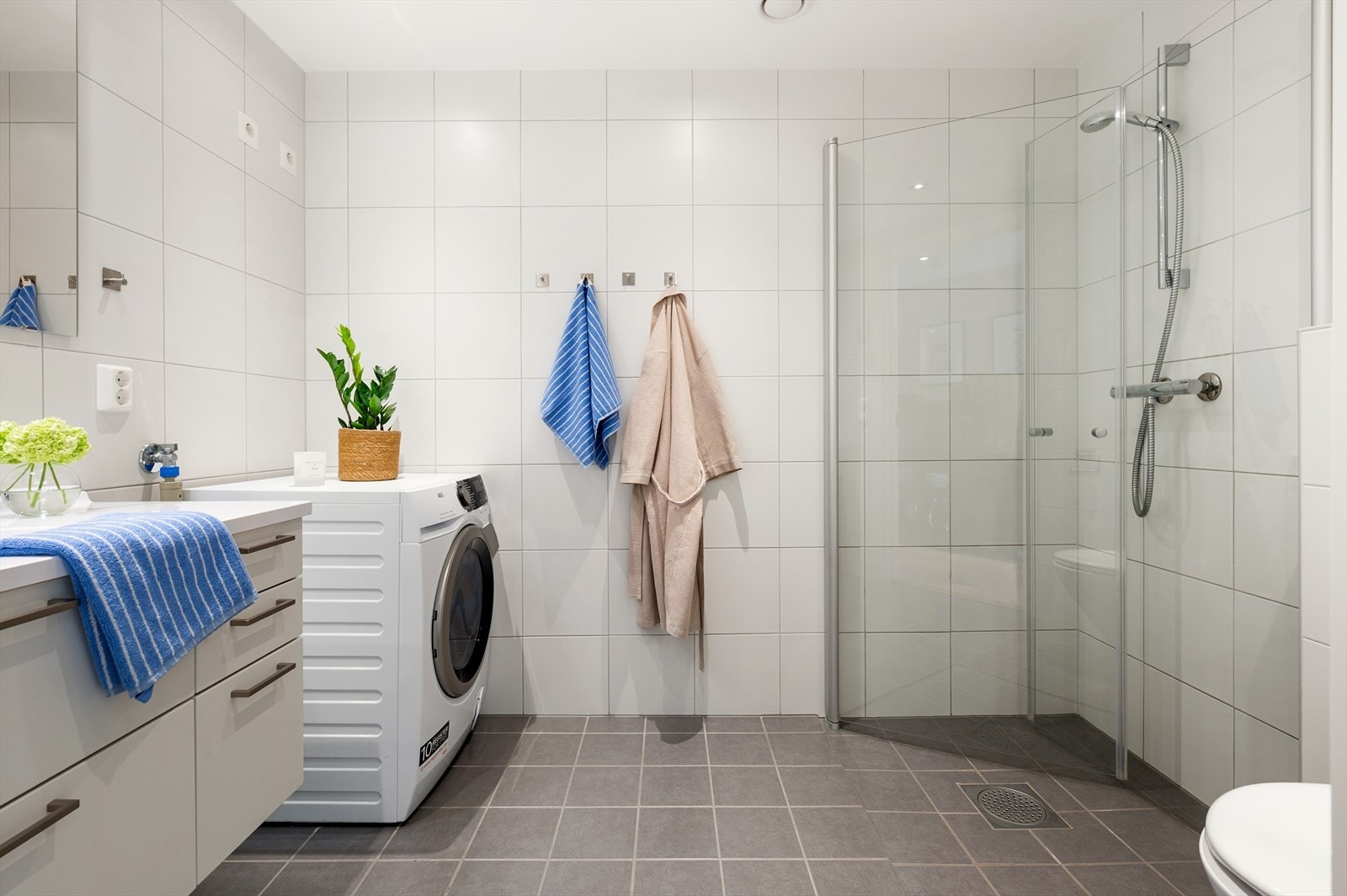 Pent og tidsriktig baderom med baderomsinnredning, vegghengt toalett, dusjhjørne med innfellbare dusjvegger og opplegg for vaskemaskin. Galleribilde