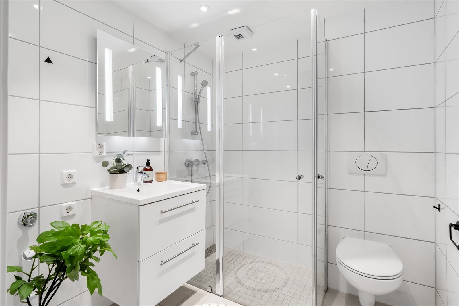 Badene har lyse fliser på gulvet og på vegger, med vannbåren gulvvarme og downlights i taket. Galleribilde