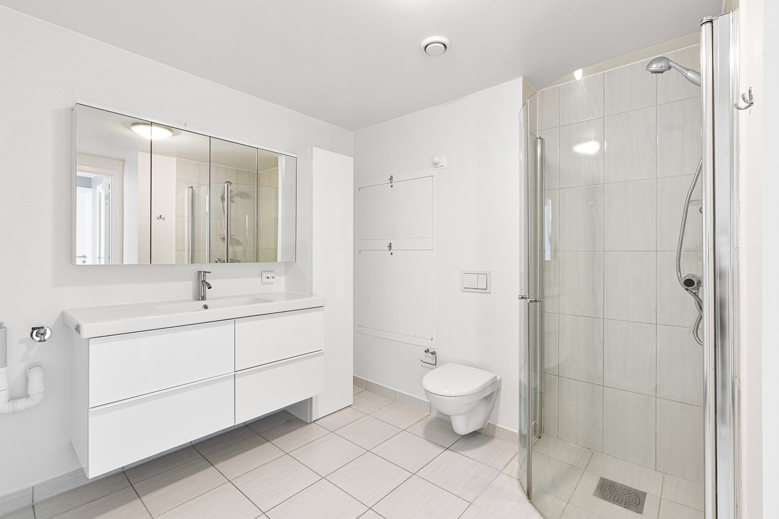 Badet har moderne innredning med to nedfelte servanter, veggmontert toalett og dusjhjørne med glassvegger. Det er også opplegg for vaskemaskin, noe som gjør rommet både funksjonelt og praktisk. Galleribilde