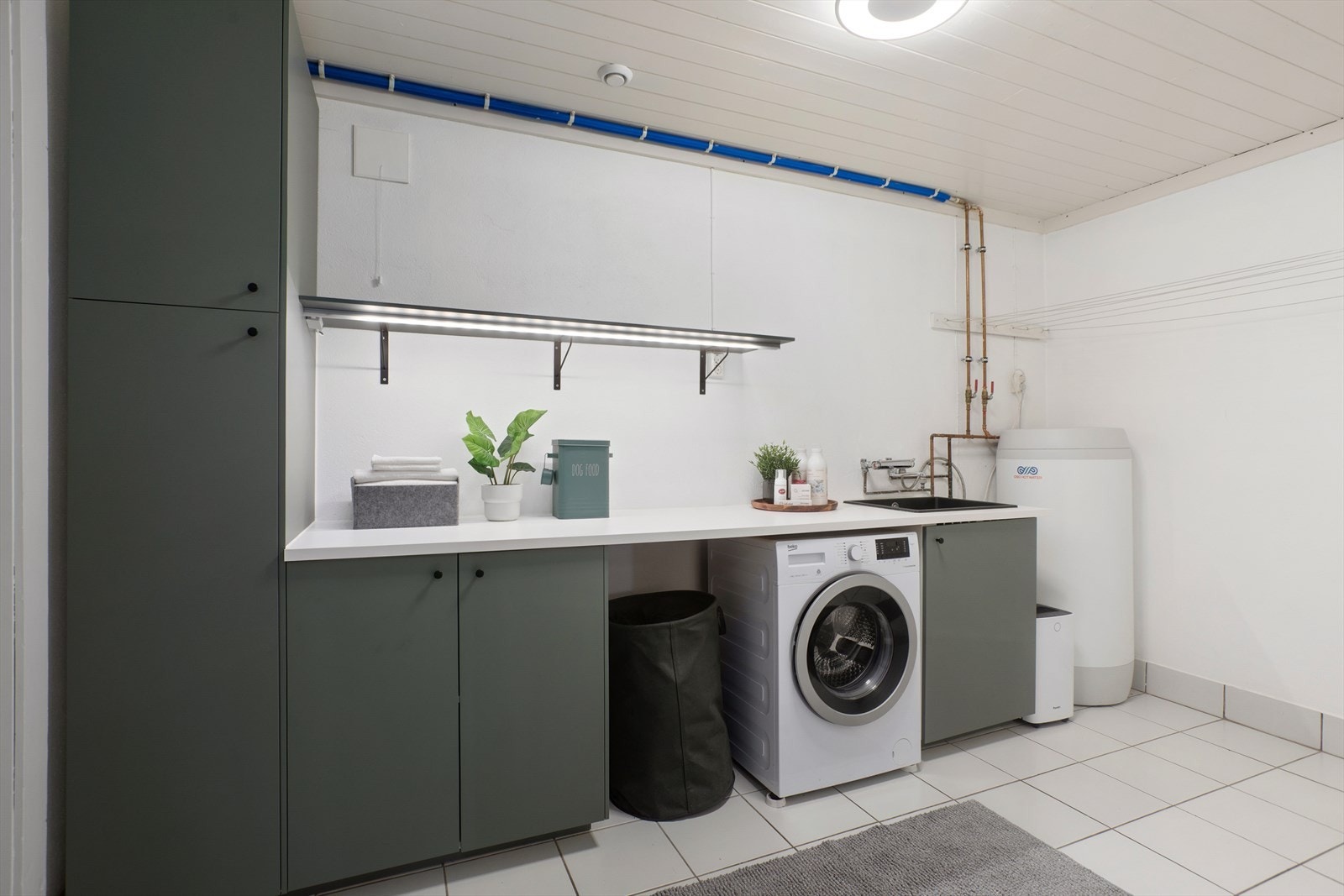 Praktisk vaskerom med flis på gulv og malte murvegger. Vaskerommet inneholder moderne innredning for både oppbevaring og nisje for vaskemaskin. Galleribilde
