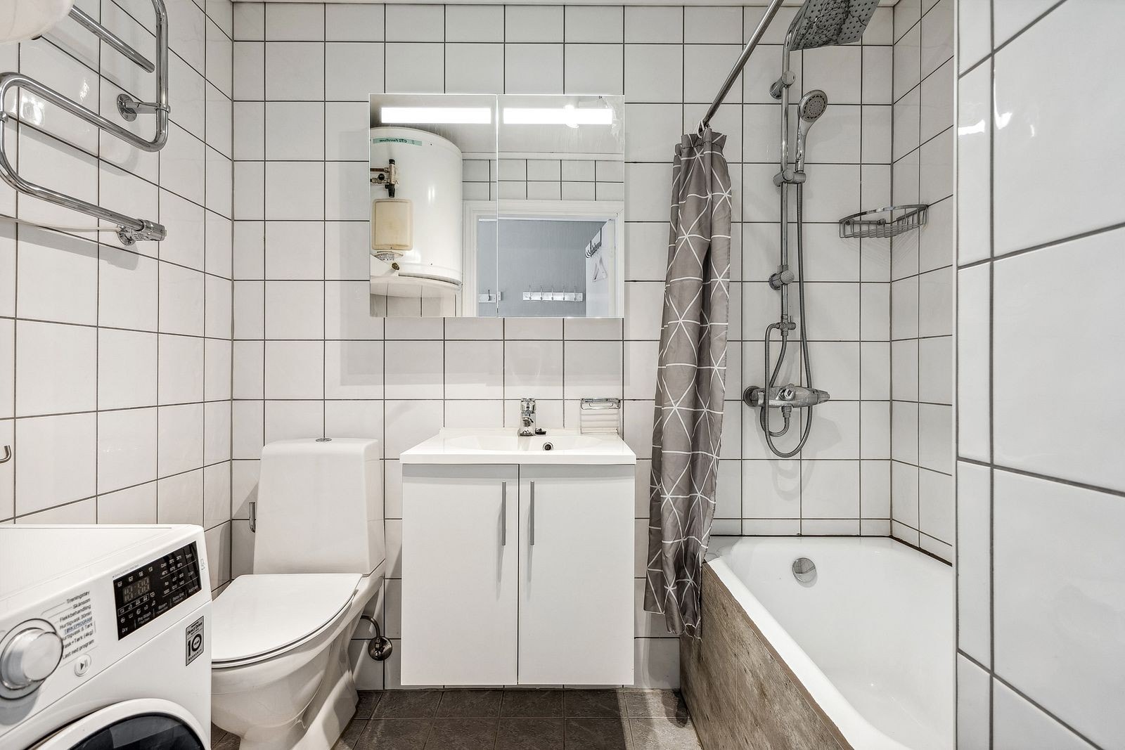 Bad med toalett, vask, dusj i badekar, vaskemaskin og tørkestativ på vegg. Galleribilde