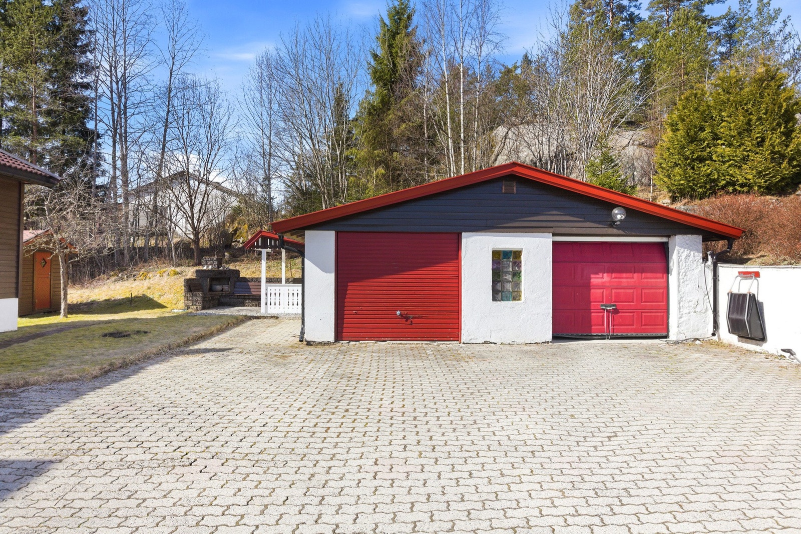 Steinsbelagt gårdsplass med halvpart av garasje, grillområde og plen. Galleribilde