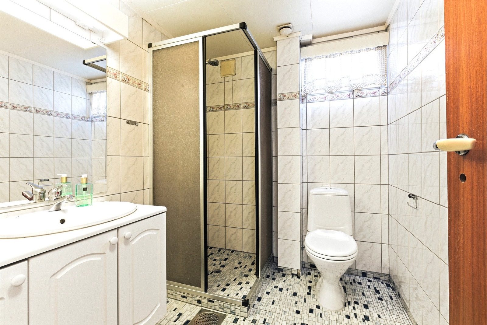 Badet har flislagte vegger og gulv, dusjkabinett, toalett og servant med underskap. Galleribilde