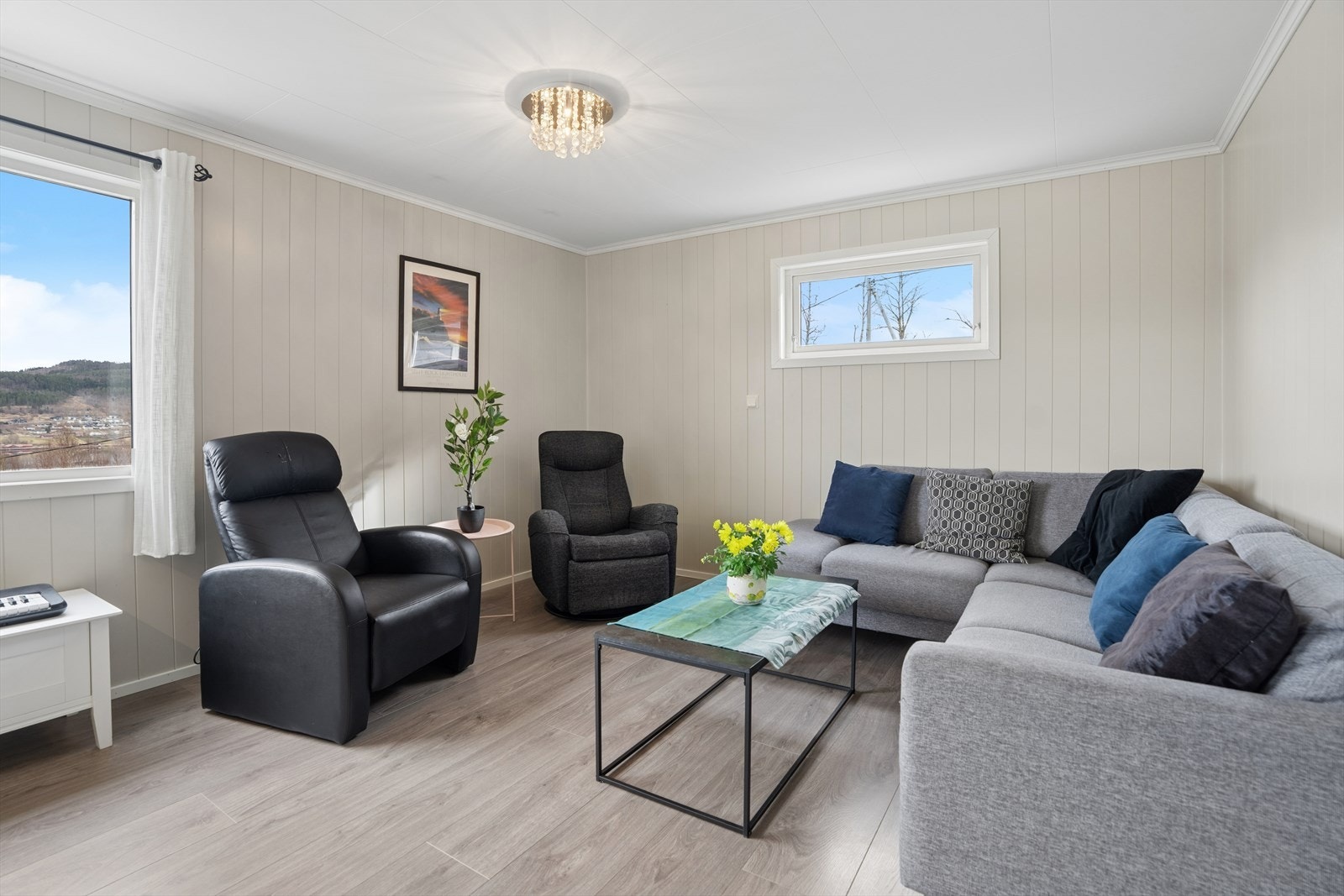 Et lyst og luftig oppholdsrom med vegger kledd i panelplater og laminat på gulvet. Galleribilde