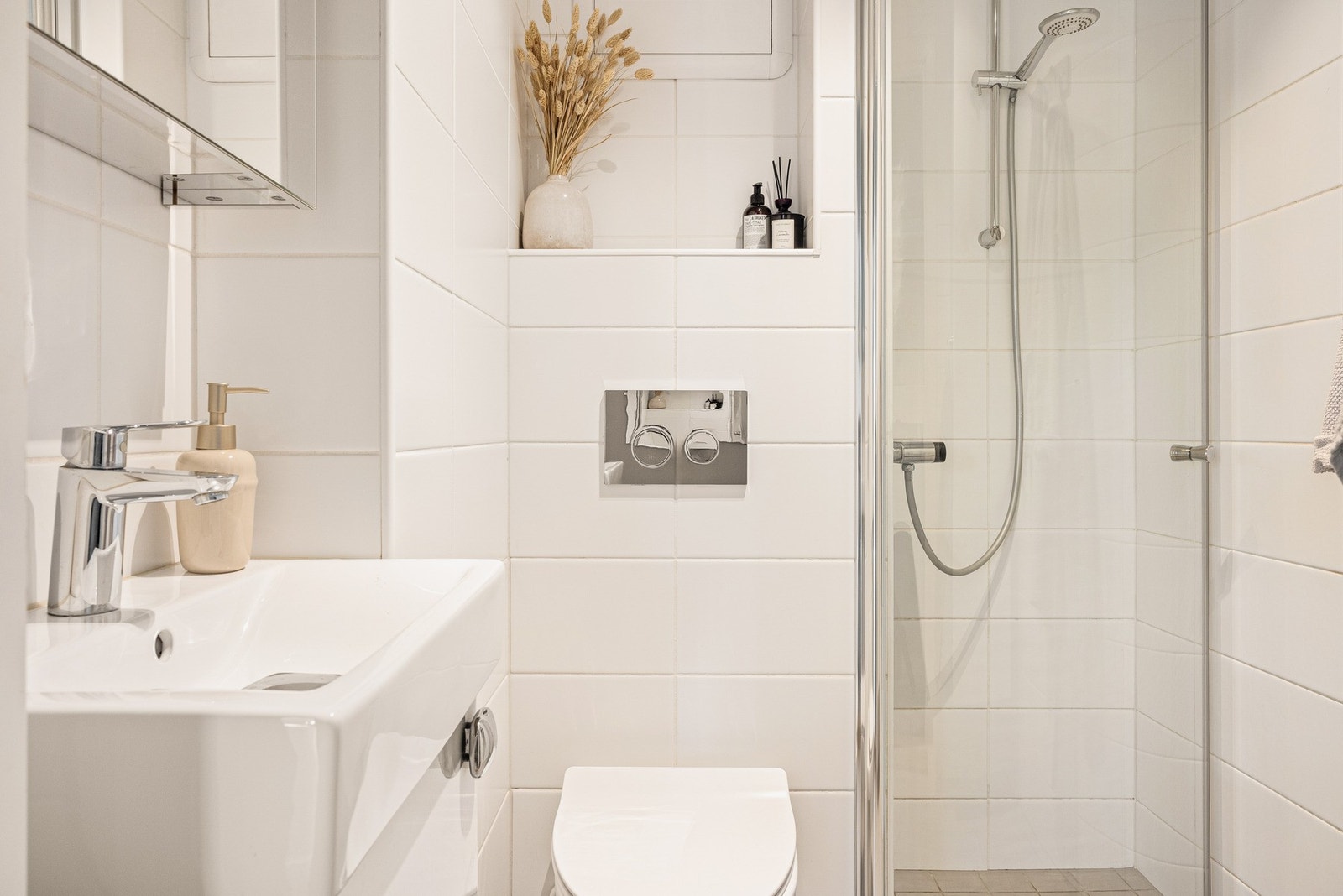 Badet er godt plassutnyttet med integrerte varmekabler, vegghengt toalett, dusjhjørne med dusjgarnityr, baderomsmøblement med speil og skap til oppbevaring. Galleribilde