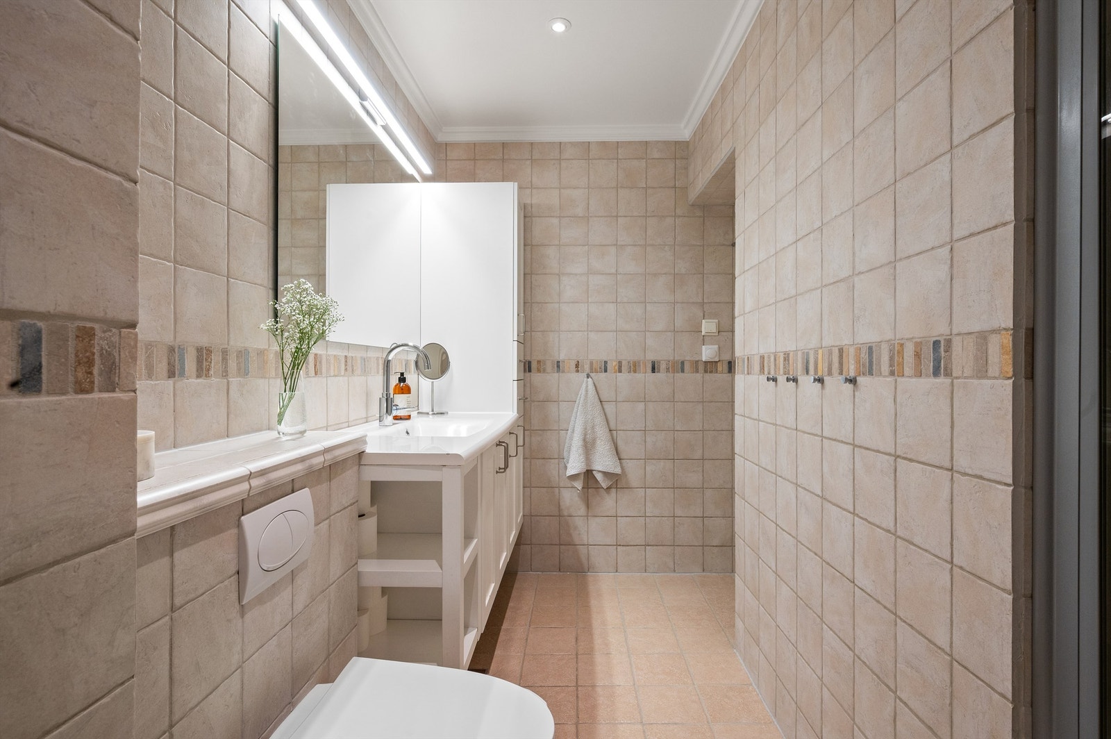 Badet er innredet med vegghengt toalett, servant med underskap og innfelte LED-downlights i taket. Galleribilde