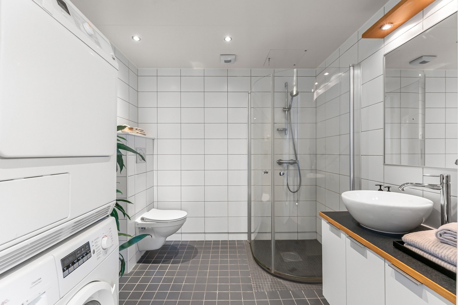 Badet er fra byggeår og har flislagte gulv og vegger med varmekabler i gulvet. Rommet har downlights i taket og avtrekk via balansert ventilasjonsanlegg. Galleribilde
