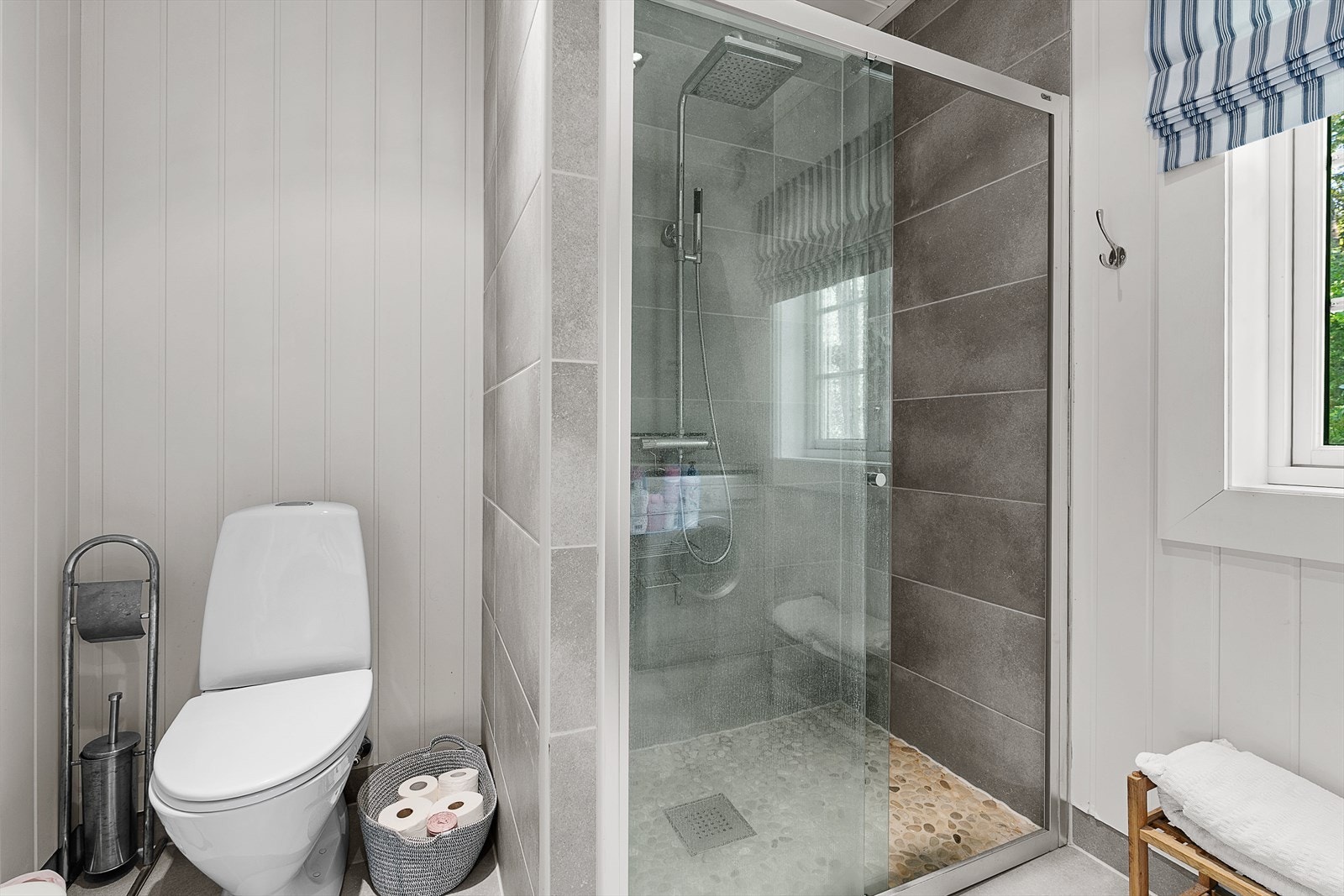Badet har lysmalt panel på veggene, grå fliser i dusjsonen og lysegrå fliser på gulv med gulvvarme. Galleribilde
