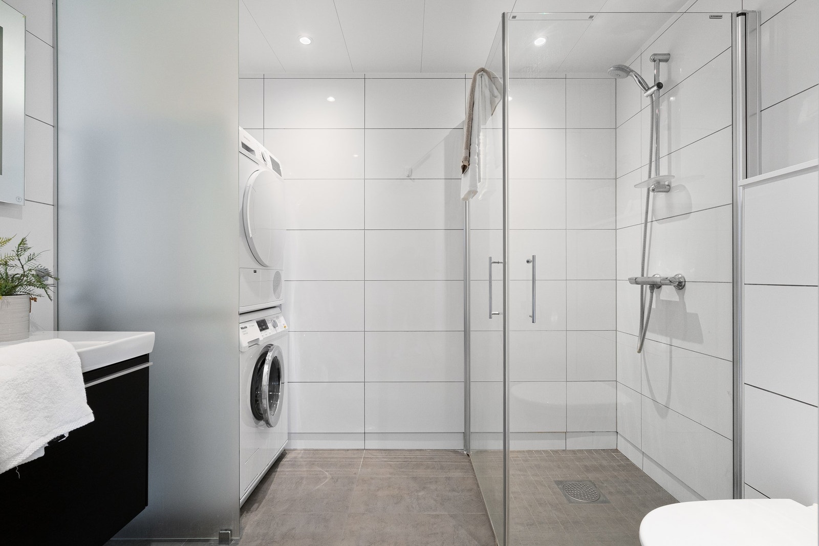 Det er dusjhjørne med innfellbare dører, vegghengt toalett og servant med oppbevaringsplass i skuffer. Opplegg for vaskemaskin og plass til tørketrommel, som er smart plassert bak en frostet glassvegg. Spotter i tak Galleribilde