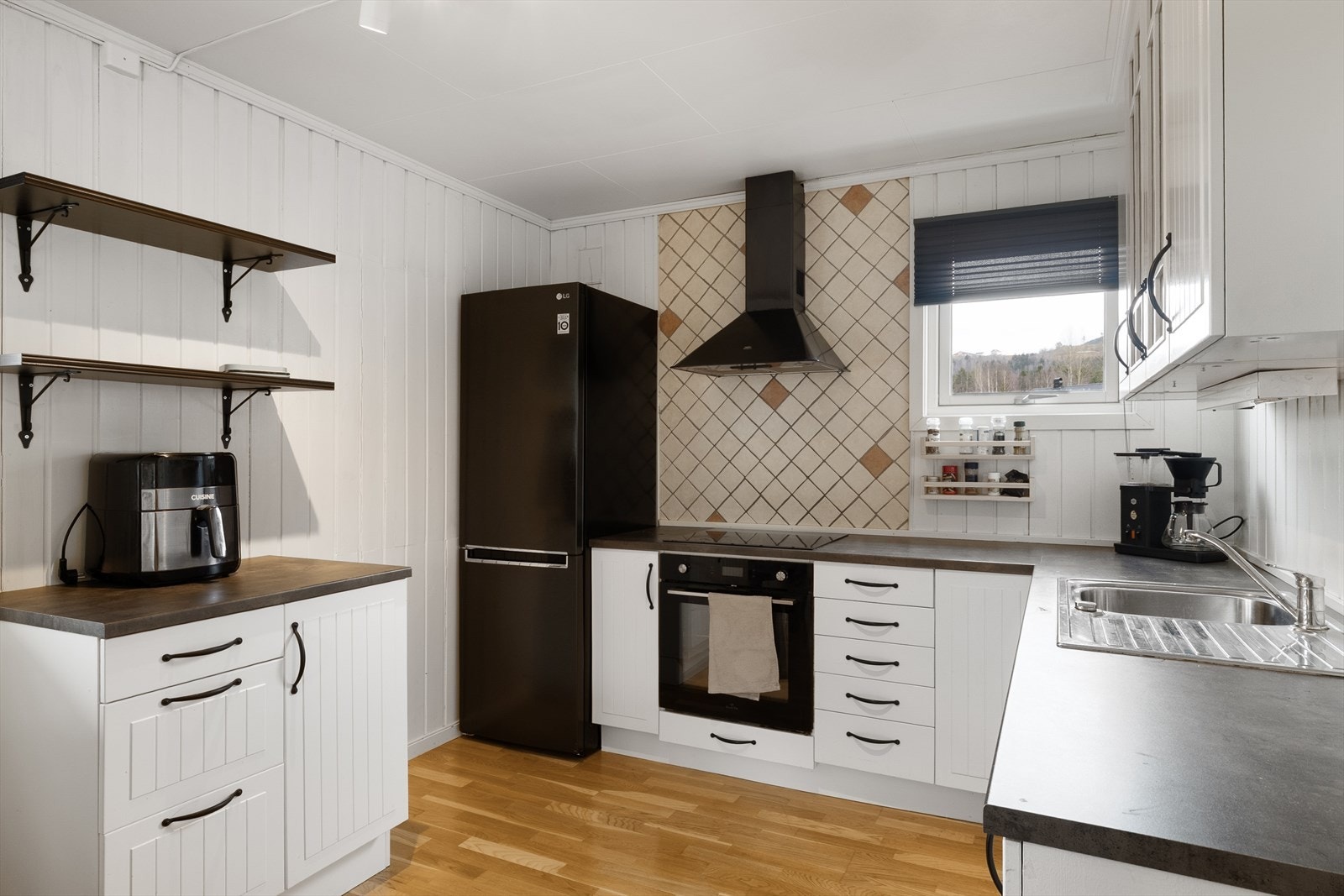 Pent kjøkken med profilerte, malte fronter og en laminert benkeplate med nedfelt vaskekum. Galleribilde