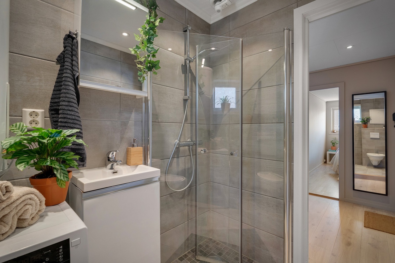 Badet er helfliset og utstyrt med vaskemaskin, varmtvannstank, heldekkende servant, veggehengt toalett, inntrekksbare dusjdører, samt speil med belysning. Galleribilde