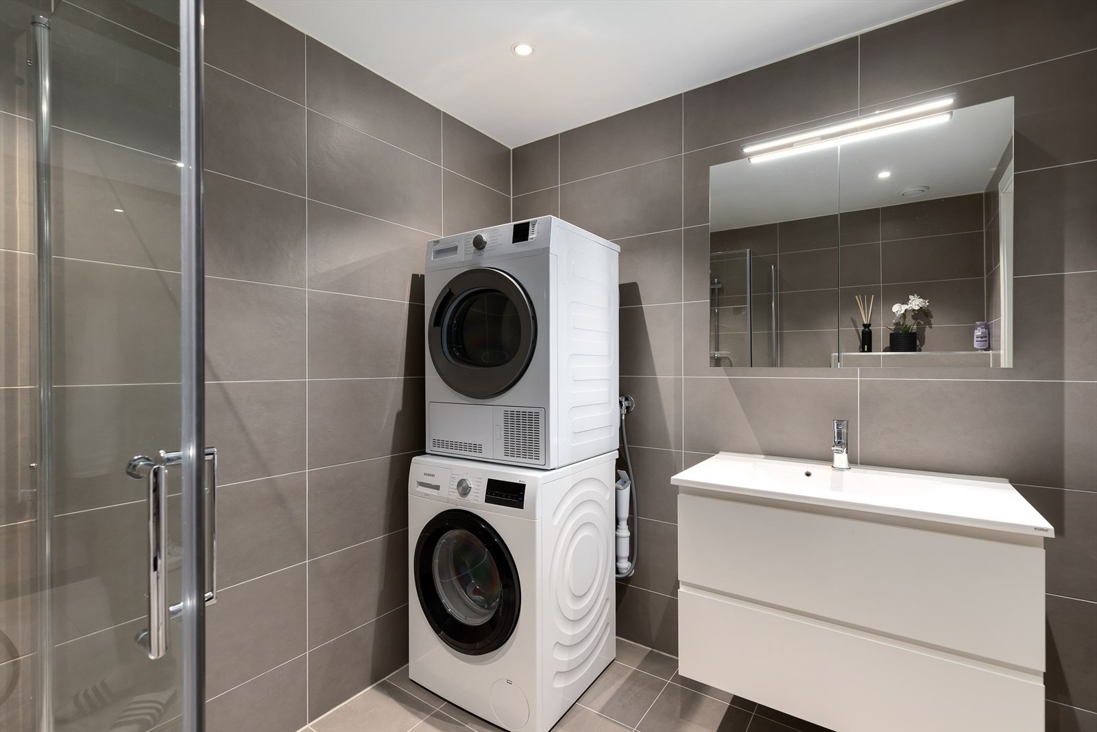 Badet består av 80 cm servant med skuffer, dusjhjørne med innfellbare glassvegger og vegghengt toalett. Opplegg for vaskemaskin. Galleribilde