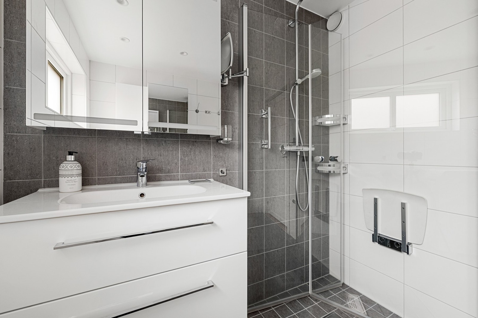 Videre er badet utstyrt med dusj med glassdører, servant med innredning og speil med belysning. Galleribilde