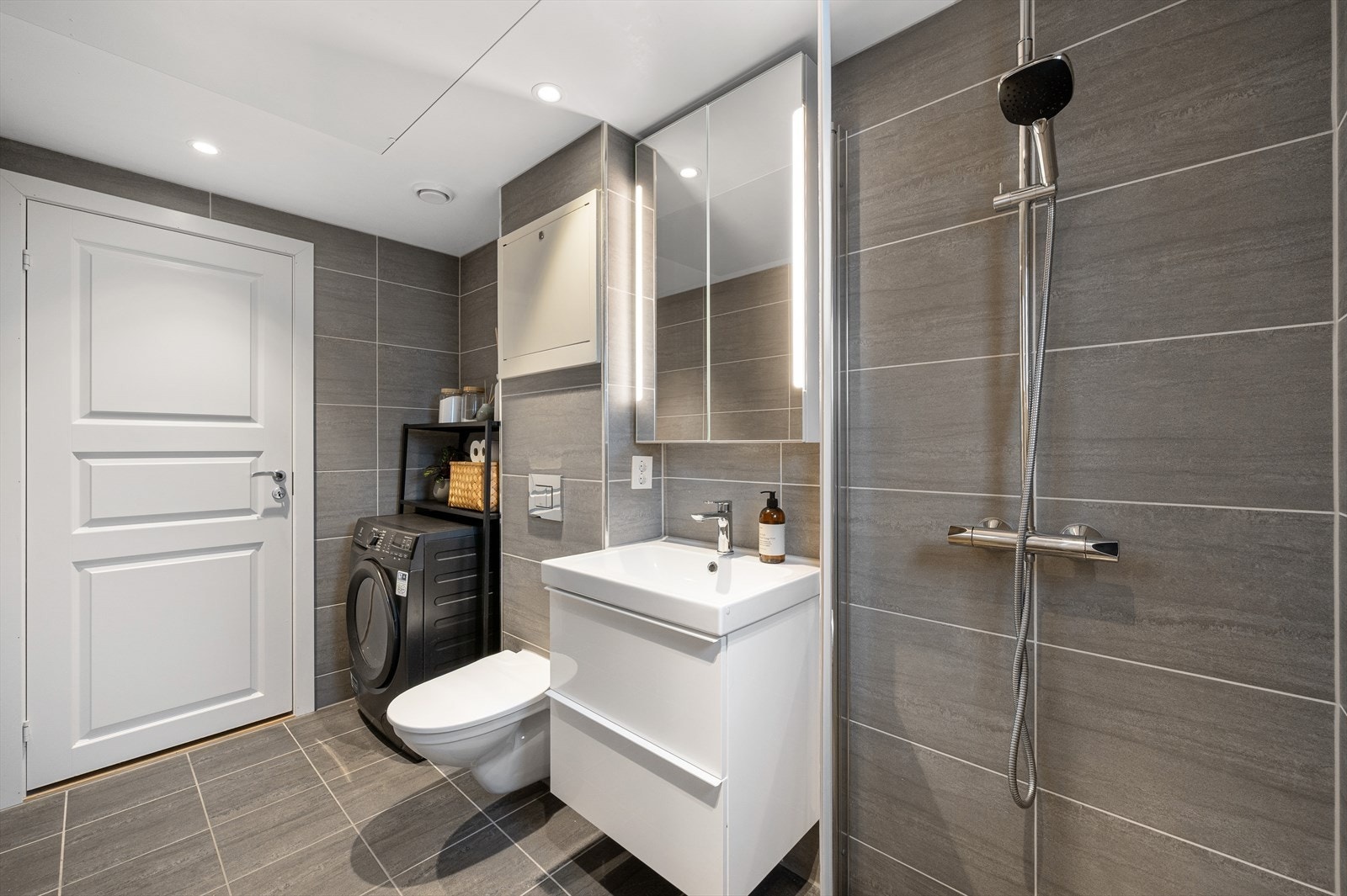 Badet er innredet med vegghengt toalett, dusjhjørne m/glassdør, opplegg for vaskemaskin samt servant med innredning, speilskap og belysning. Galleribilde