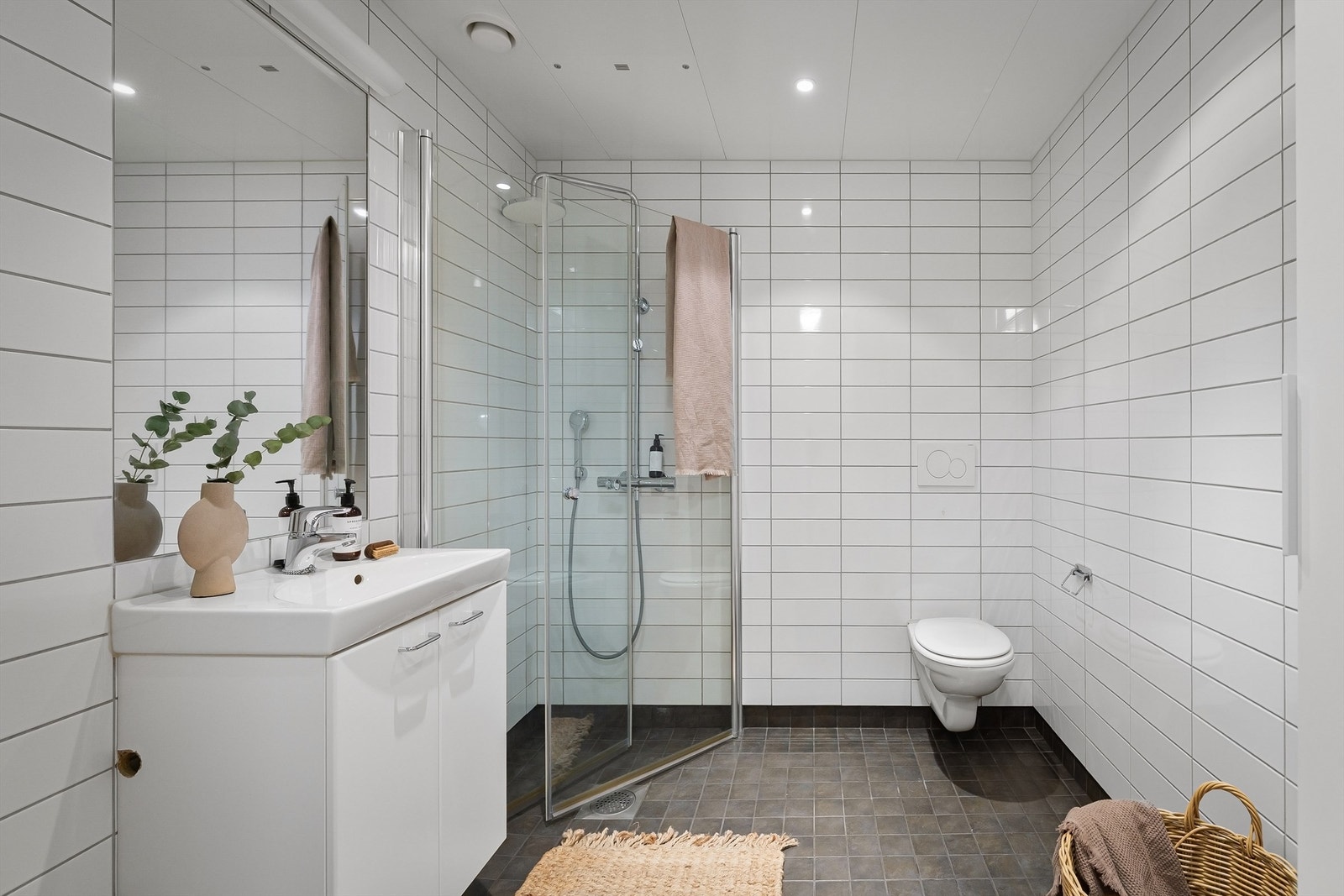 Innbydende og meget romslig bad med hvite fliser på vegg, gråmelerte fliser med varme i gulv og downlights i himling Galleribilde
