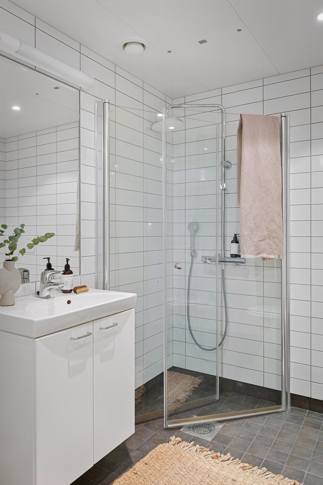 Badet er utstyrt med vegghengt toalett, dusjhjørne med innfellbare glassdører og dusjsett med rainshower samt servant med skapinnredning og speil med belysning over Galleribilde