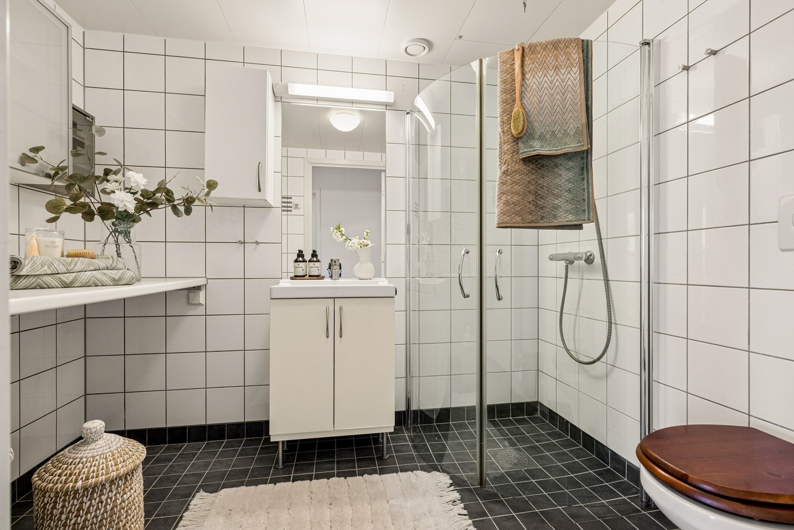 Flislagt bad med elektriske varmekabler i gulvet, vegghengt toalett og dusjhjørne med innfellbare glassdører. Galleribilde