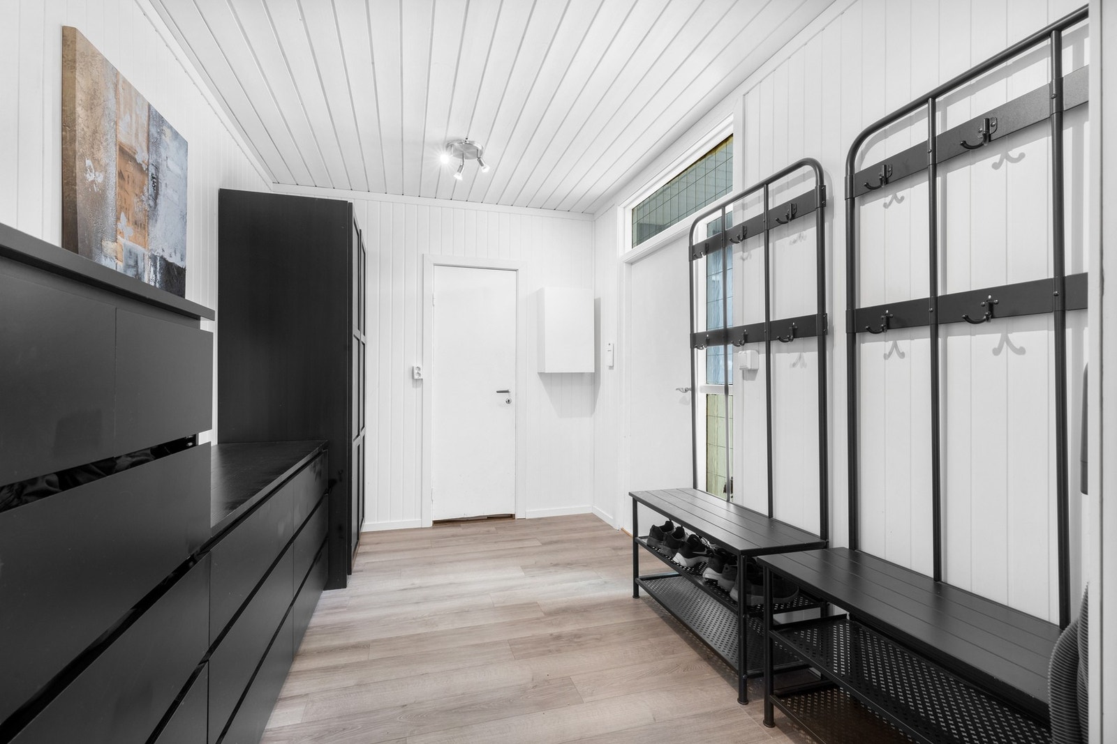 Entreen har et sort garderobeskap med profilerte fronter, samt god plass til annet møblement. Det er dør inn til et garderoberom. Galleribilde
