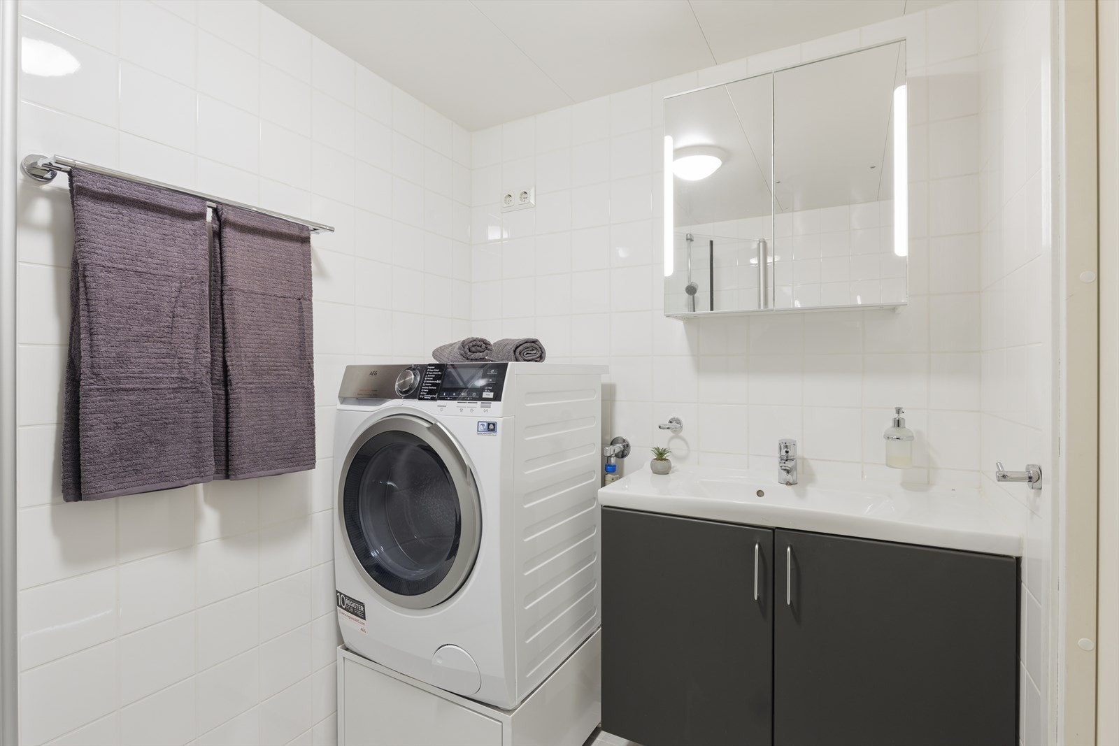 Det er god plass til vaskemaskin på badet, og praktisk oppbevaringsplass under maskinen gir ekstra rom for orden og lagring. Galleribilde