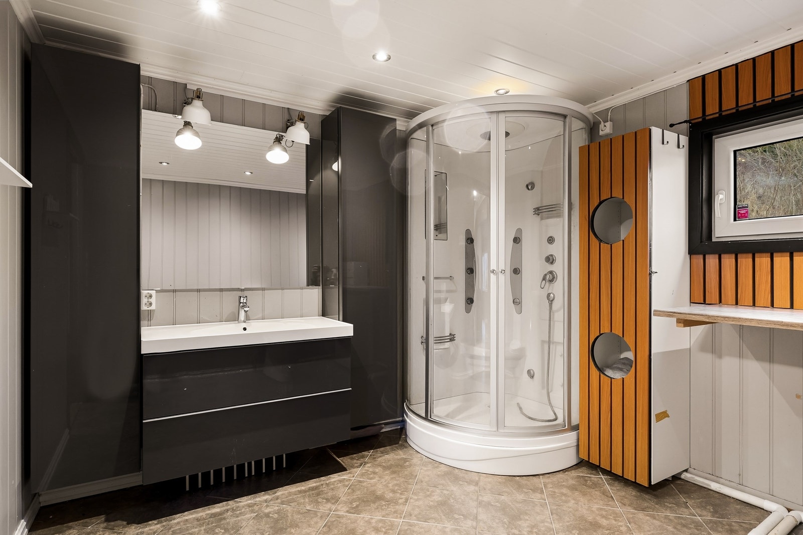 Badet har flislagt gulv med varmekabler, dusjkabinett og servant i seksjon. Det er også opplegg til vaskemaskin. Galleribilde