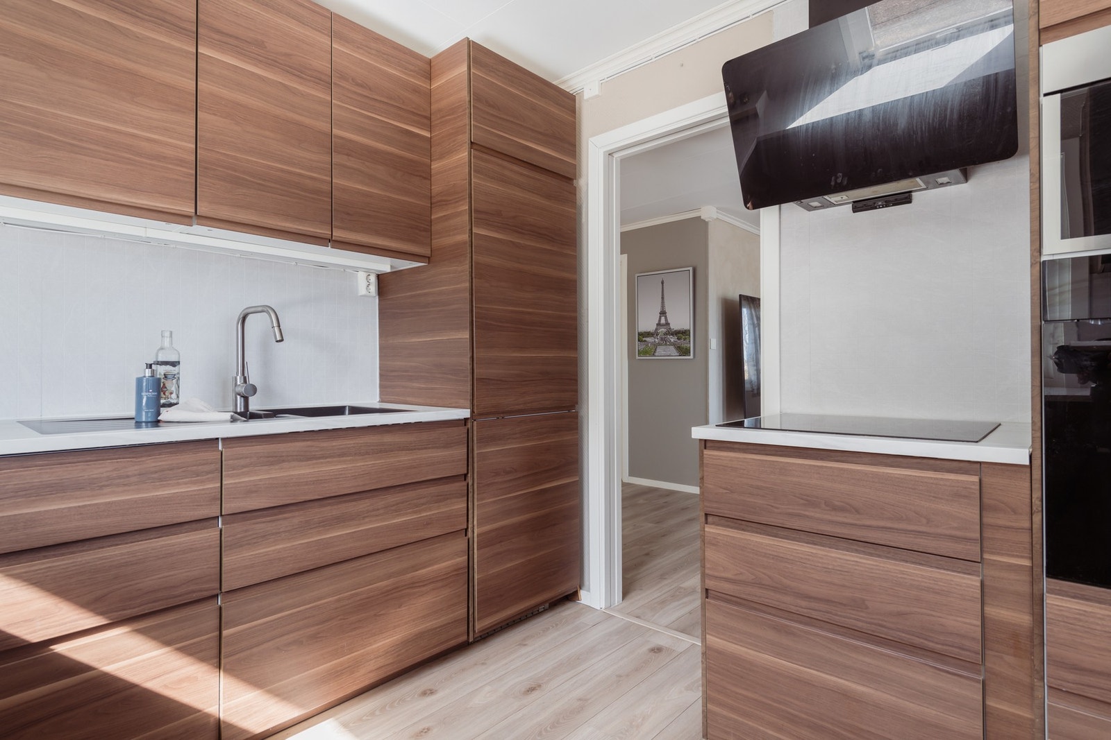 Over benken er det belysning og lysegrå plater i flismønster, og over kokesonen har kjøkkenet en komfyrvakt og en ventilator. Galleribilde