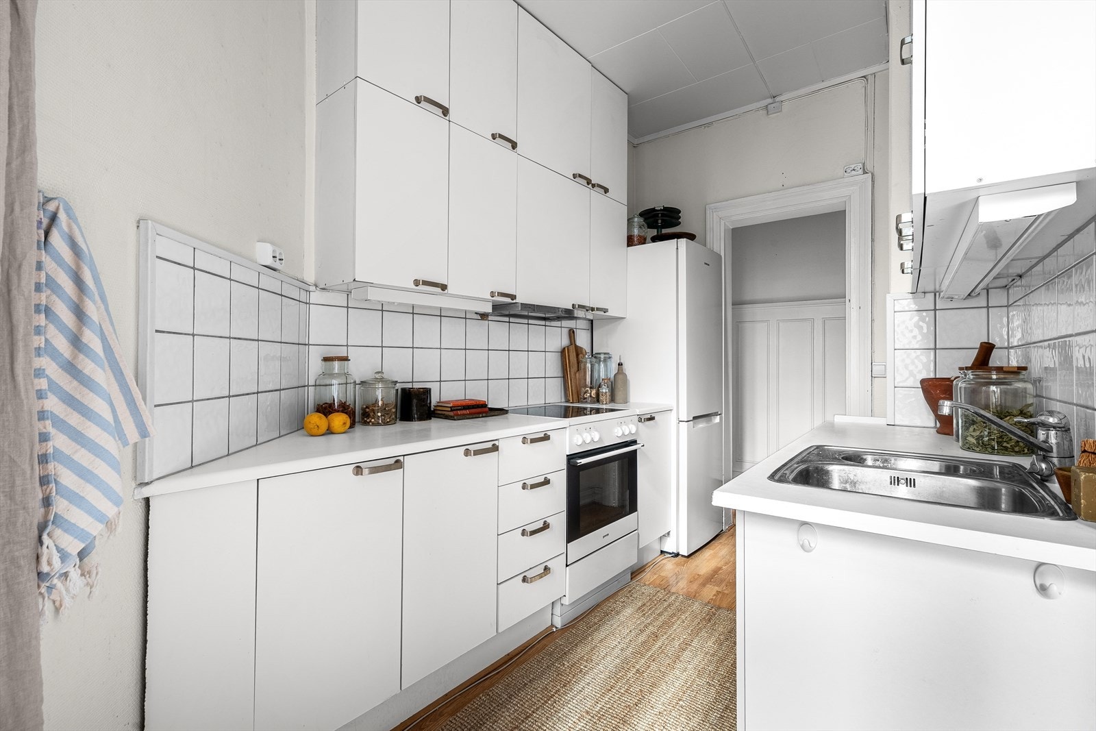 Enkel innredning med slette fronter, fliser og belysning over laminat benkeplate med oppvaskkum og blandebatteri. Galleribilde