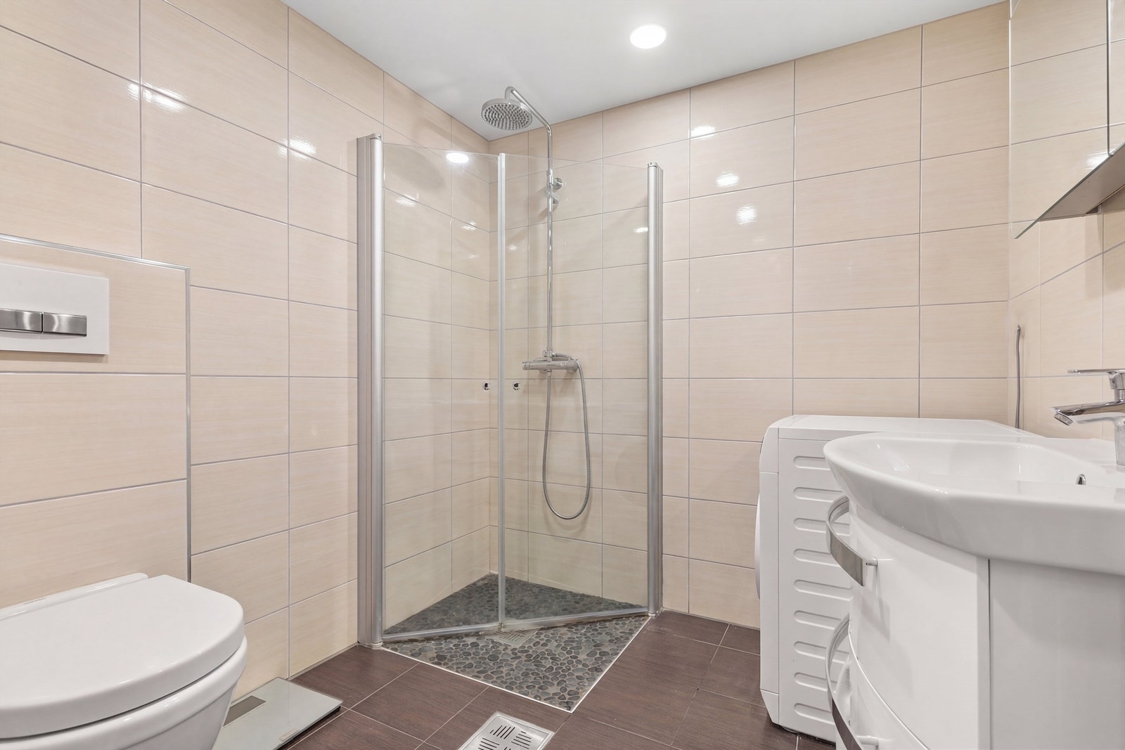 Badet er flislagt på gulv og vegger med elektrisk gulvvarme. Badet er innredet med vegghengt klosett, servant med innredning, speilskap med lys og dusjhjørne med svingbare glassdører. Opplegg og plass for vaskemaskin og tørketrommel. Mekanisk avtrekk. Galleribilde