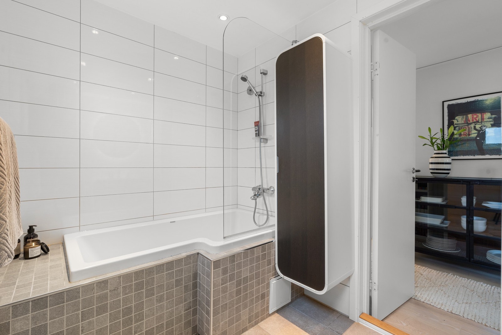 Badet har innebygd badekar med dusjdør i glass og skap for lagring av baderomsartikler Galleribilde