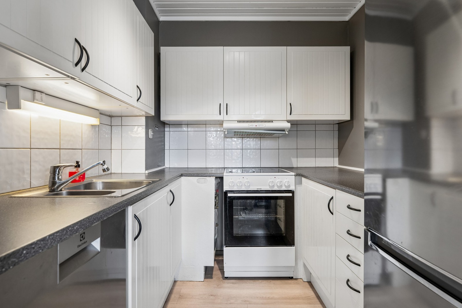 Kjøkkenet har innredning fra IKEA med profilerte fronter, laminert benkeplate og flislagt område over benk for enkel rengjøring. Galleribilde