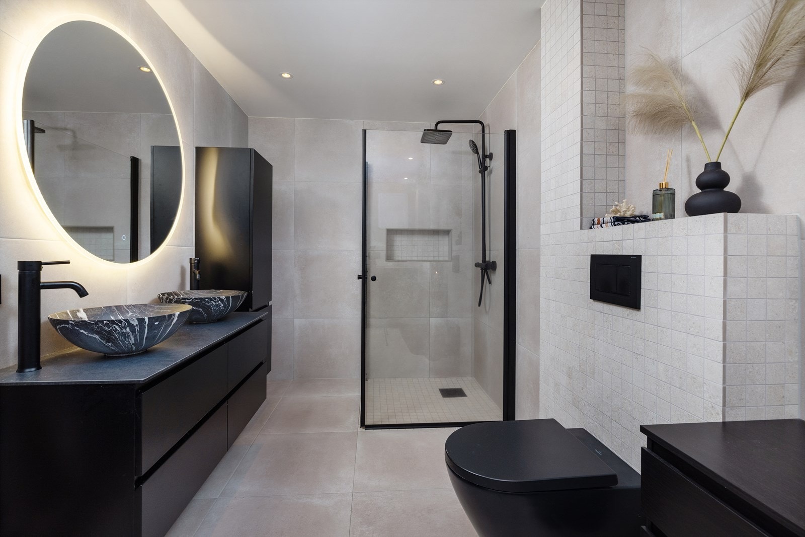 Badet har store lyse fliser på vegger og gulv, gulvvarme, speil m/belysning, og downlights i taket. God oppbevaringsplass og doble servanter. Galleribilde