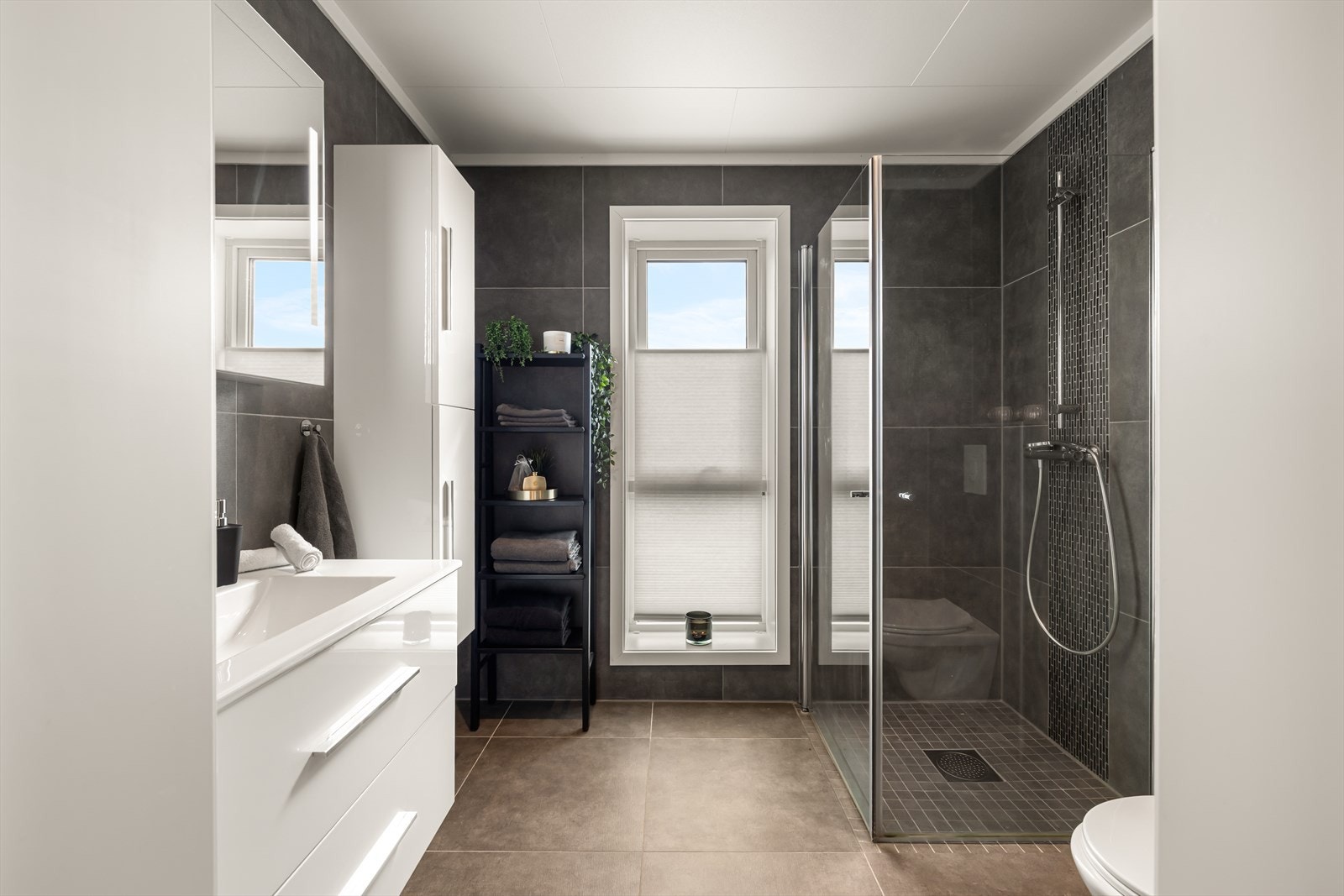 Badet har innredning med nedfelt servant, veggmontert toalett, dusjvegger/hjørne og opplegg for vaskemaskin. Galleribilde