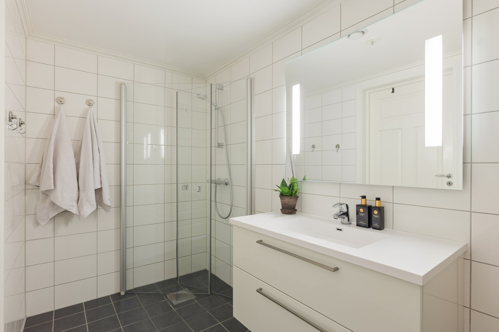 Badet i hovedetasjen holder samme tidløse stil og uttrykk som badet i underetasjen, med lyse fliser på vegger og mørkere gulv. Galleribilde