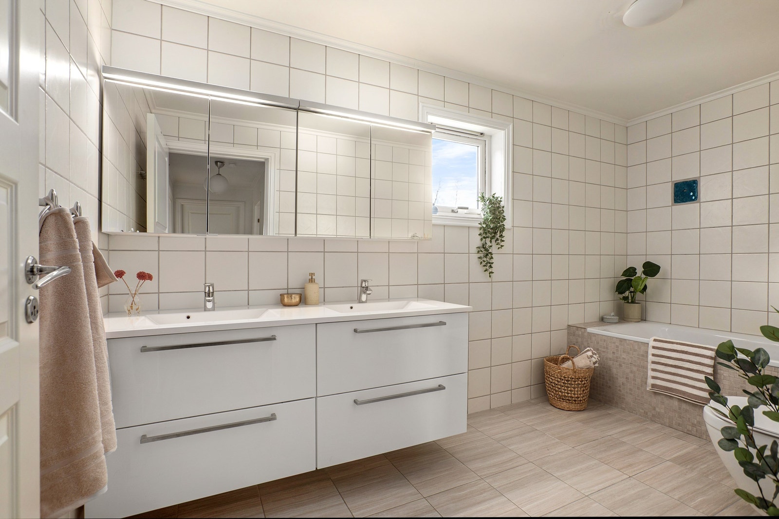 Badet er innredet med servantinnredning med dobbel servant, speilskap med belysning, badekar med vegghengt armatur og vegghengt toalett Galleribilde