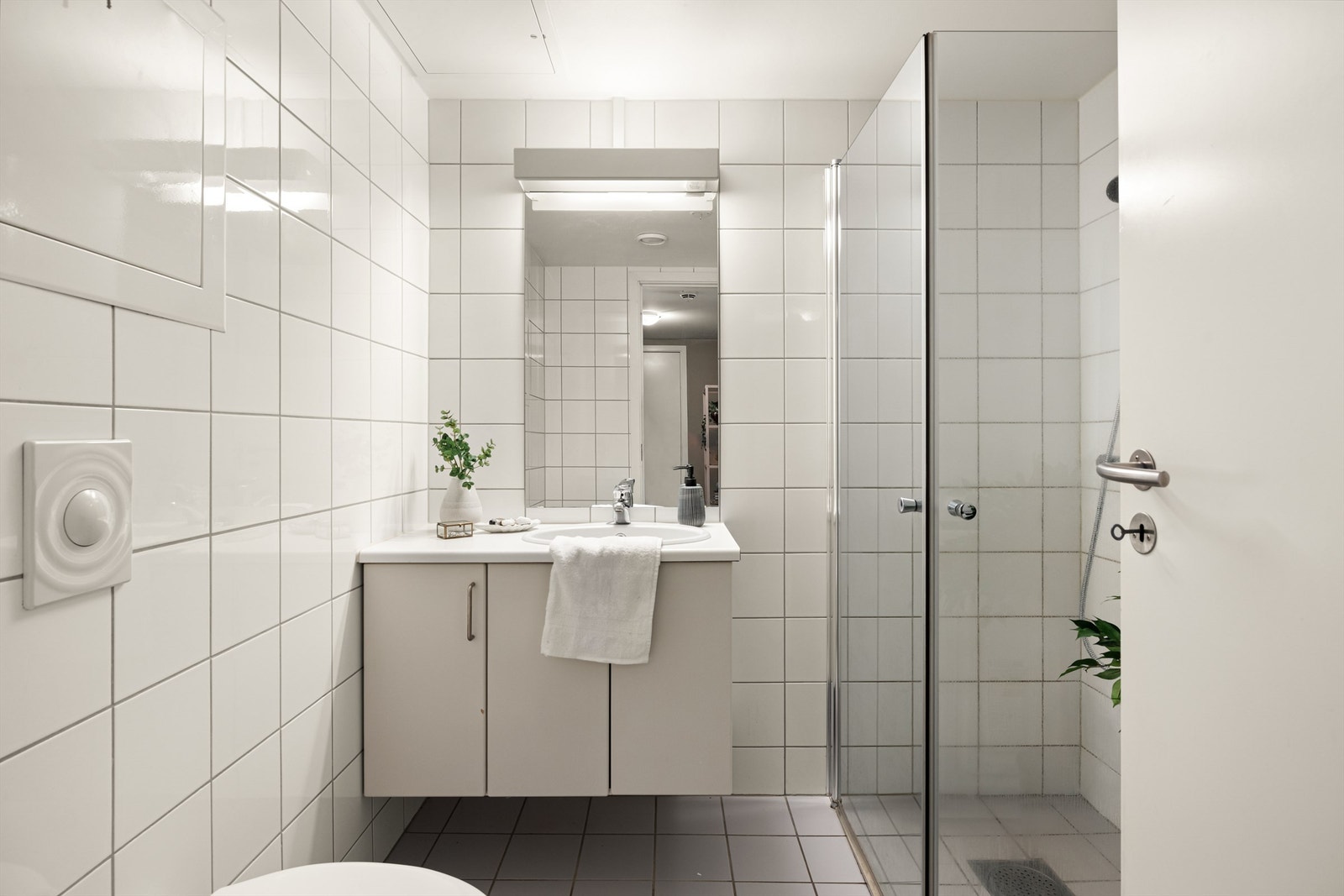 Badet er utstyrt med vegghengt toalett, servant med underskap og dusjhjørne med innfellbare glassdører. Galleribilde