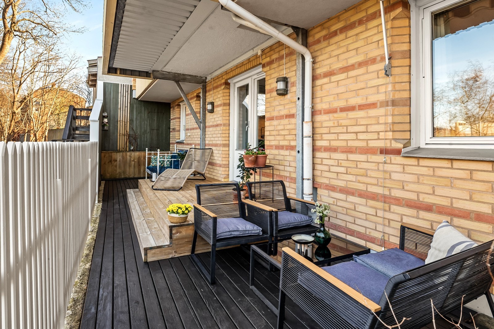 Verandaen er en lun og hyggelig plass med overbygg, terrassebord på gulv og utvidet vegg i hjørne for skjerming. Galleribilde