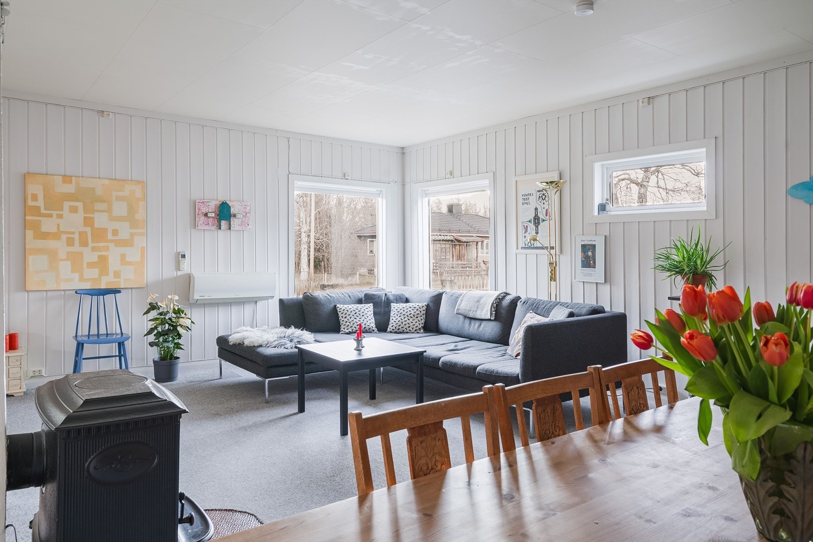 Lys og romslig stue med teppe på gulv og lysmalt panel på veggene. Galleribilde