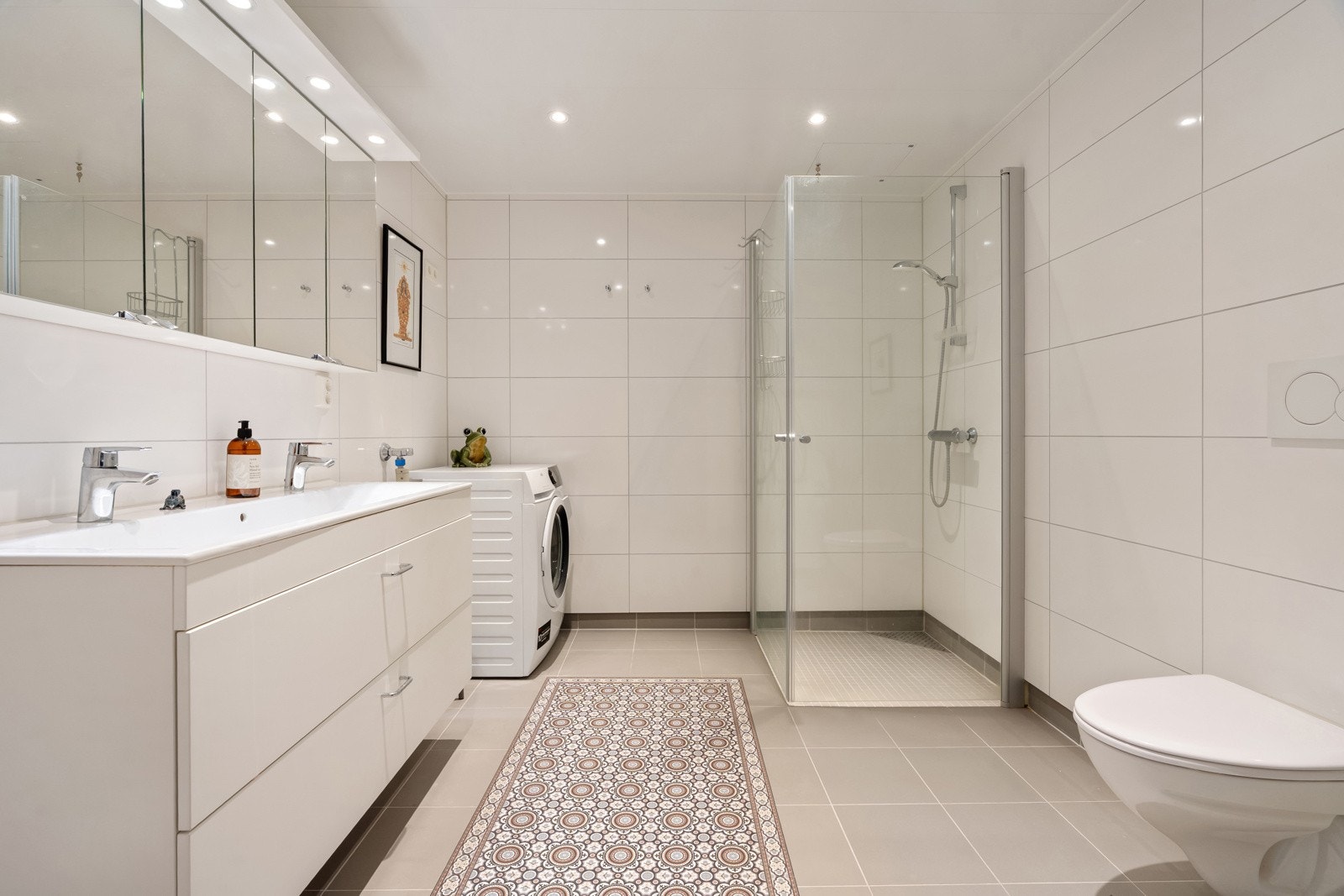 Flislagt bad med praktisk innredning, speilskap, dusjhjørne og vegghengt wc.