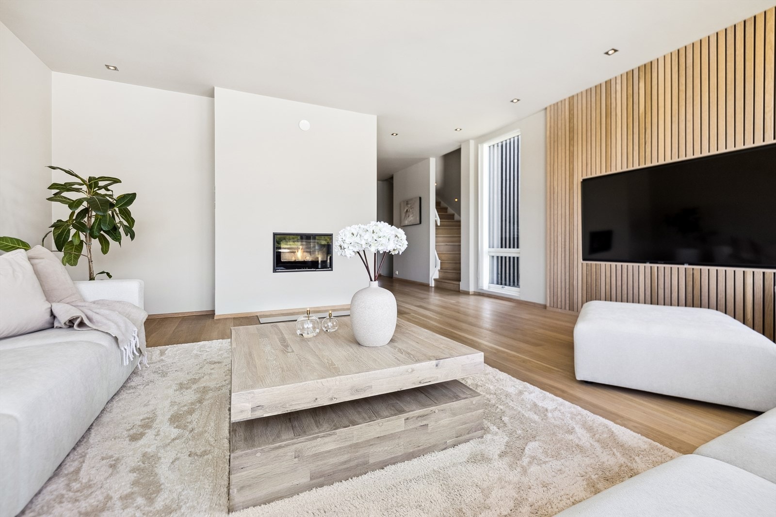 Stilfull stue med gjennomført design - her møtes varme og eleganse. Den innebygde peisen i veggen skaper en lun atmosfære, mens spilerveggen tilfører et eksklusivt og naturlig preg. Galleribilde