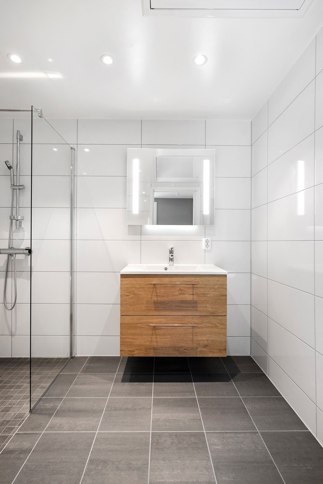 Utstyrt med vegghengt toalett, dusjhjørne med innfellbare glassvegger, samt baderomsinnredning med servant og speilløsning med LED-lys. Opplegg for vaskemaskin og tørketrommel i nisje. Galleribilde