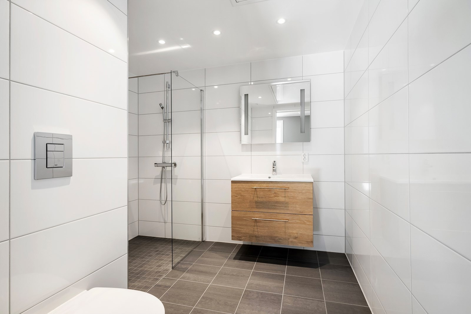Baderom med moderne standard. Flislagt gulv i antrasitt med mosaikk i dusjsonen og hvite, blanke veggfliser. LED-spotter i himling med dimmer og gulvvarme gir både komfort og stil. Galleribilde