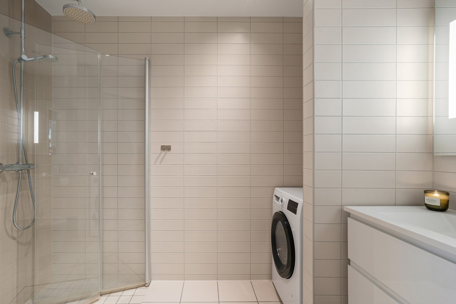 Badet er innredet med hvitt, moderne servantskap, vegghengt toalett, dushjørne med innfellbare glassvegger og regnfallsdusj, nisje for vaskemaskin og tørketrommel. Galleribilde