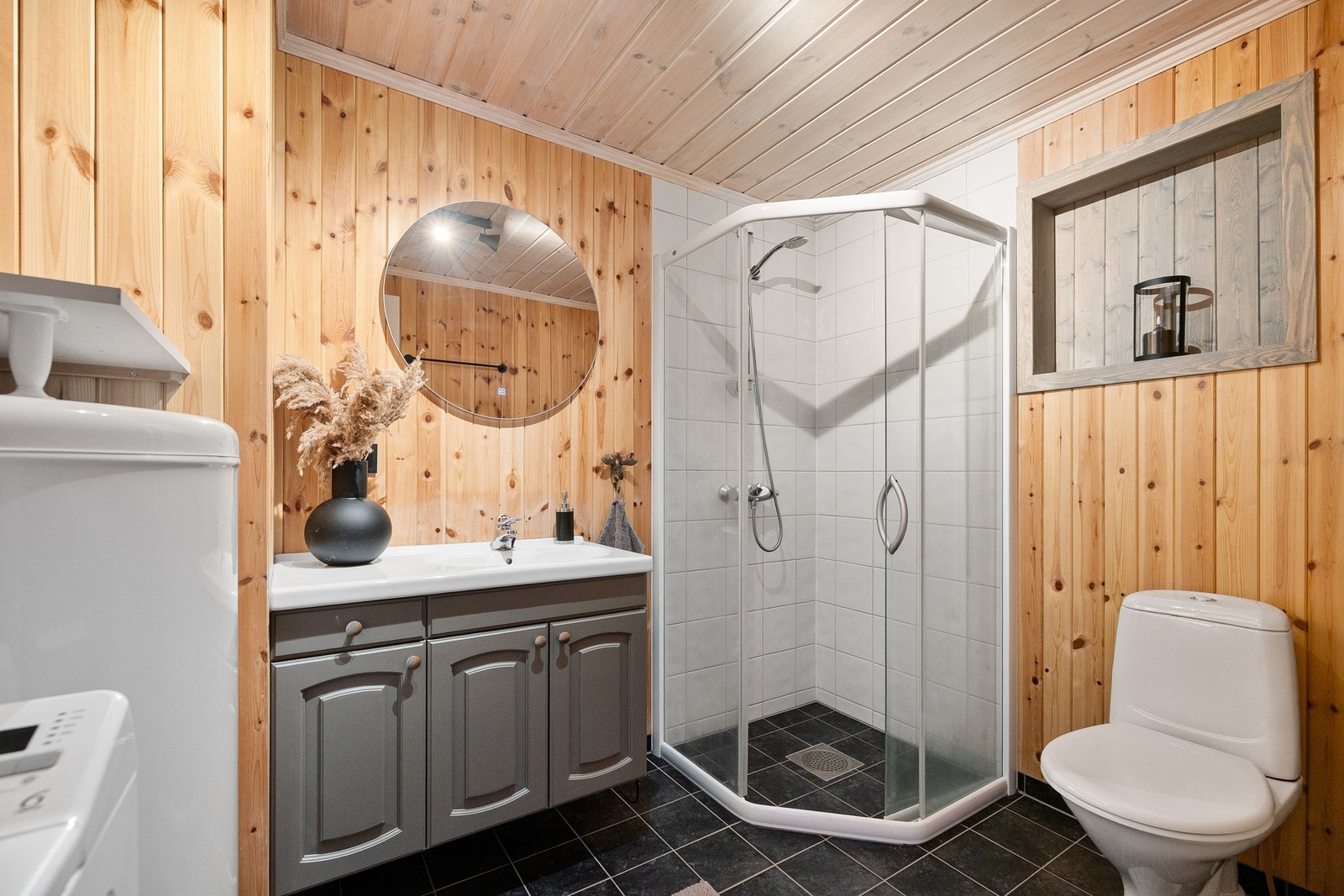 Badet har vegger med fliser i kombinasjon med panel/tømmer, og himling med panel. Rommet er innredet med nedfelt servant, toalett og dusjhjørne med dusjvegger. Galleribilde