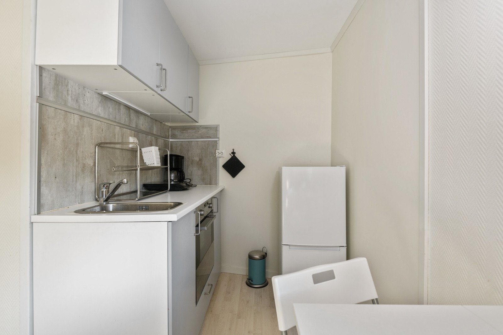 IKEA-kjøkkeninnredning fra 2018 med glatte fronter, laminert benkeplate med nedfelt oppvaskkum og plater i benkeryggen. Kjøkkenet er utstyrt med medfølgende hvitevarer som integrert stekeovn og frittstående kjøleskap med frysedel. Galleribilde