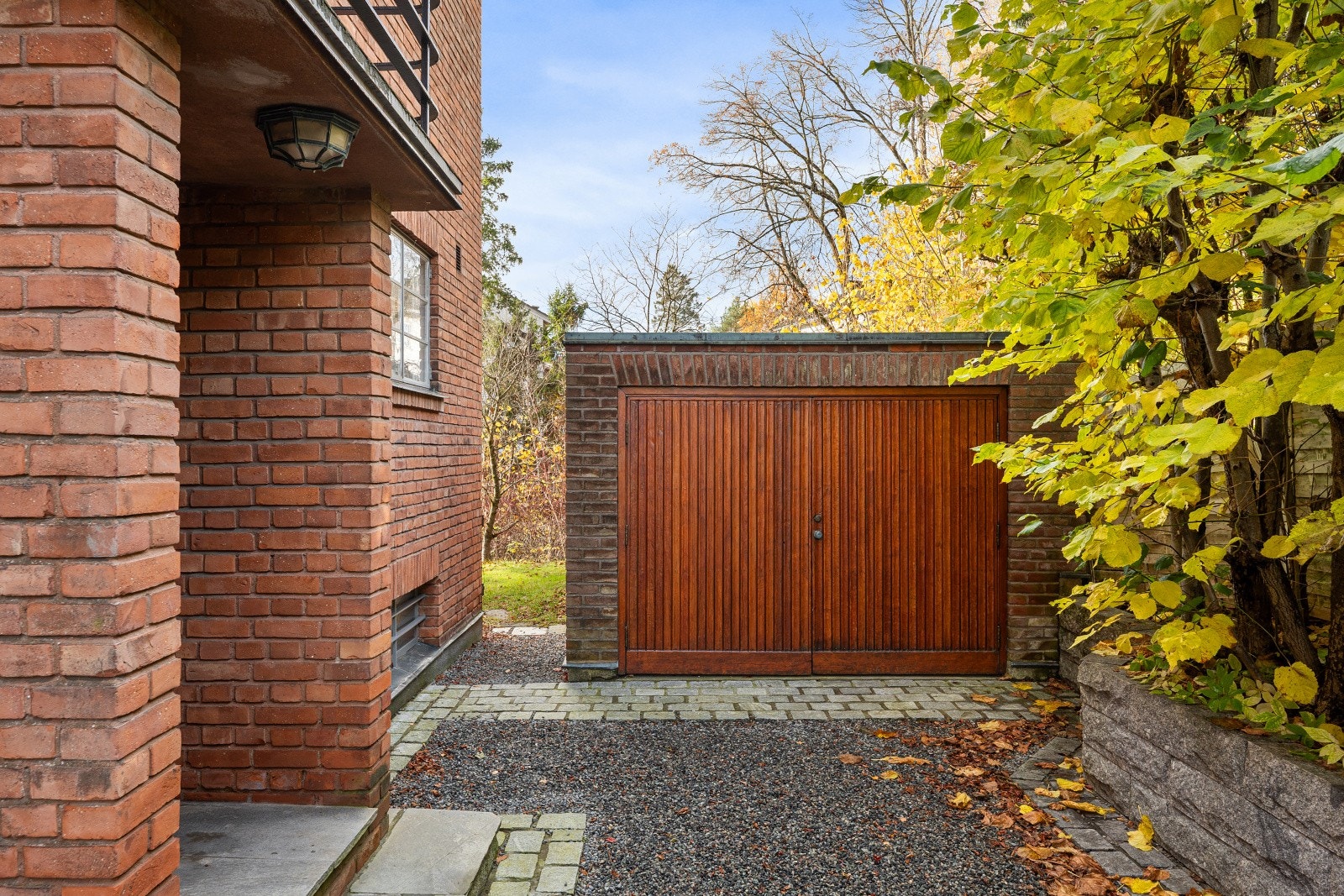 Frittstående garasje på 18 m² oppført i teglsteinsmur med garasjeport i teak. Galleribilde