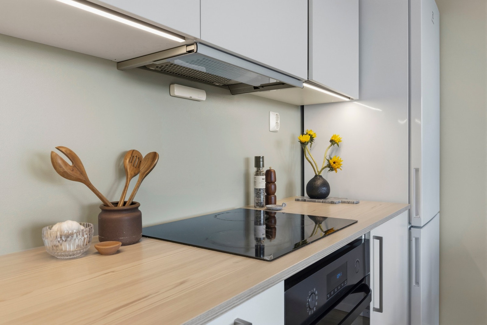 Innredningen har glatte, folierte fronter og laminat benkeplate med nedfelt kum i rustfritt stål, mens veggen over benkeplaten er malt. Galleribilde