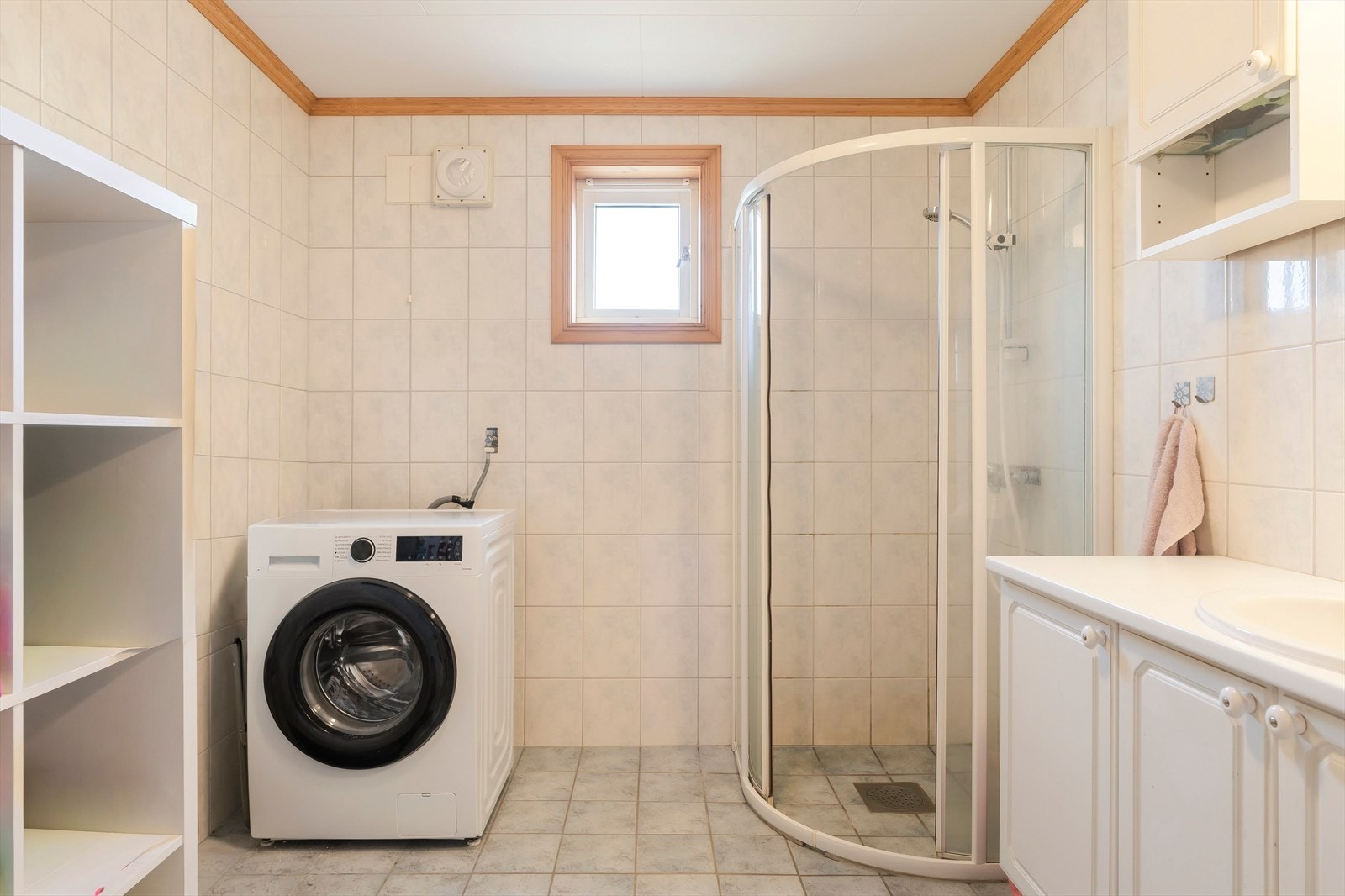 Badet er på ca. 7 m² og har en funksjonell planløsning med dusjkabinett, servantinnredning og opplegg for vaskemaskin. Rommet er flislagt på vegger og gulv, og har vindu som gir naturlig lys og mulighet for lufting. Galleribilde