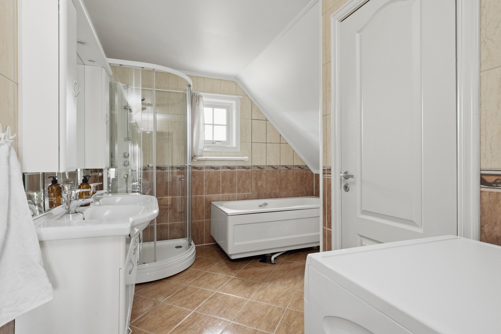 Badet ligger i loftetasjen og er fra byggeår. Rommet har flislagte vegger, gulv med varme og praktisk innredning med dusjkabinett, badekar, toalett og opplegg for vaskemaskin. Galleribilde