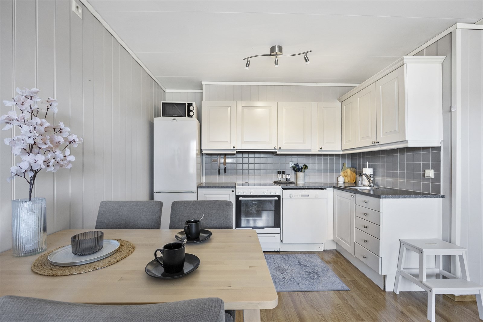 Veggene over benken er kledd med grå fliser, og under overskapene er det montert god arbeidsbelysning. Videre er kjøkkenet utstyrt med ventilator, benkestikk og opplegg for oppvaskmaskin. Galleribilde